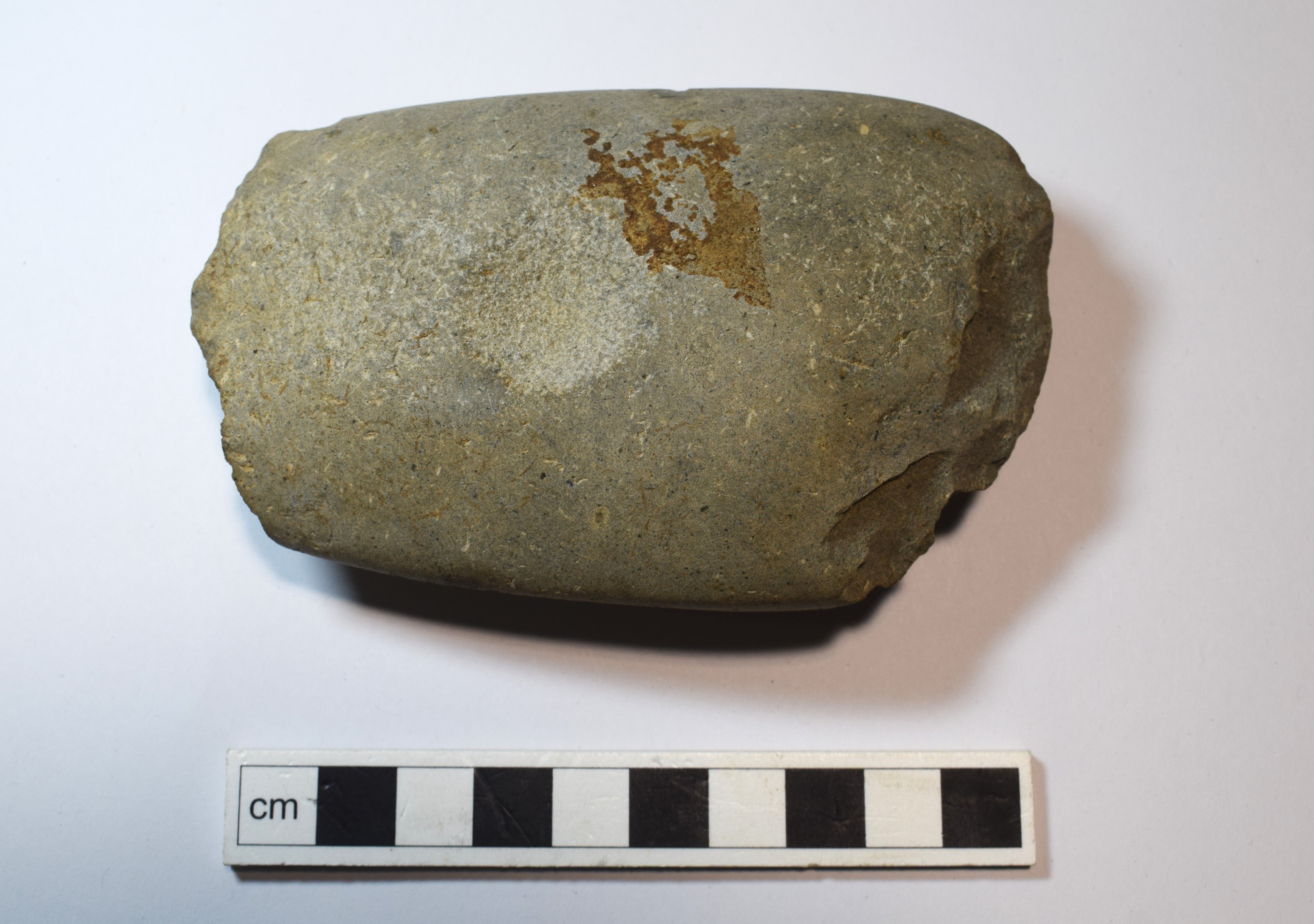 A grey-blue Langdale axe fragment on a white background with scale.