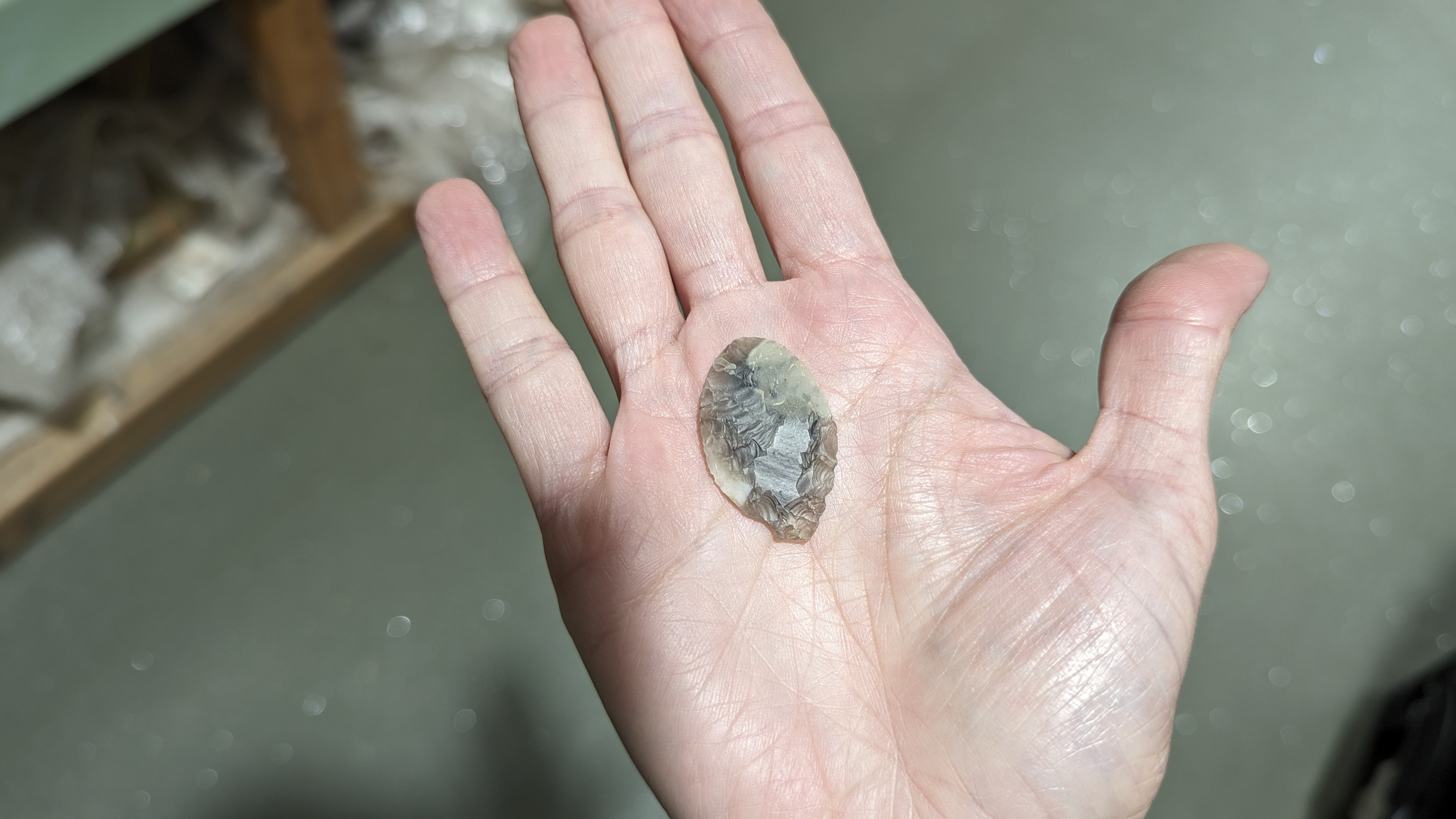 Grey, flint arrowhead held in the palm of a hand.