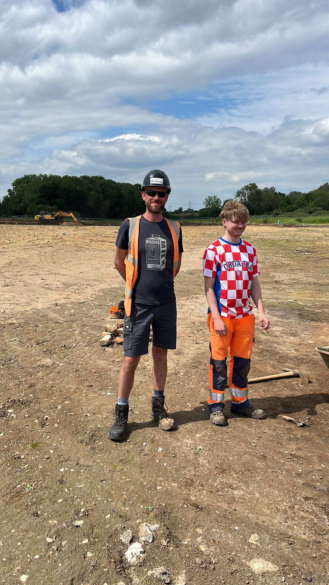 Two archaeologists are on site in shorts and short-sleeved tops.
