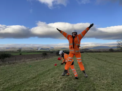 Two members of the OA team jumping up and down on a beautiful sunny day with snowy hills in the background.