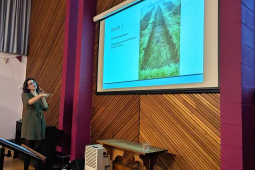 A female archaeologist delivers a PowerPoint presentation on an excavation site.