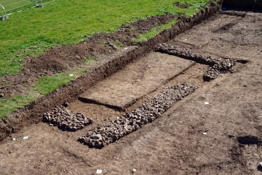 Partially exposed stone foundations of a square Roman building at the edge of the excavation site.