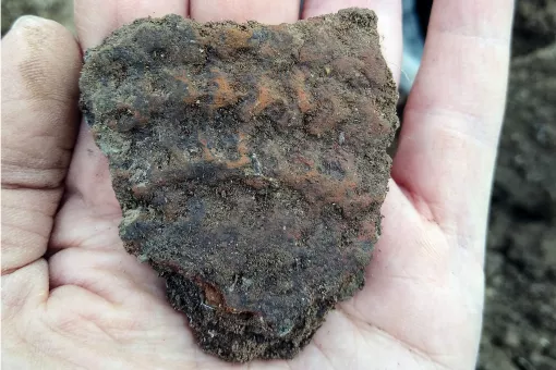 A close up of a hand holding a fragment of decorated Prehistoric pottery