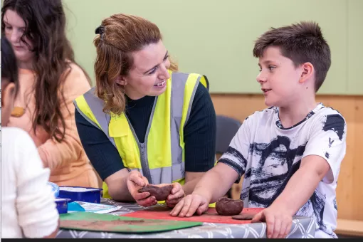 A female archaeologist teaches a young boy how to make small clay pots 