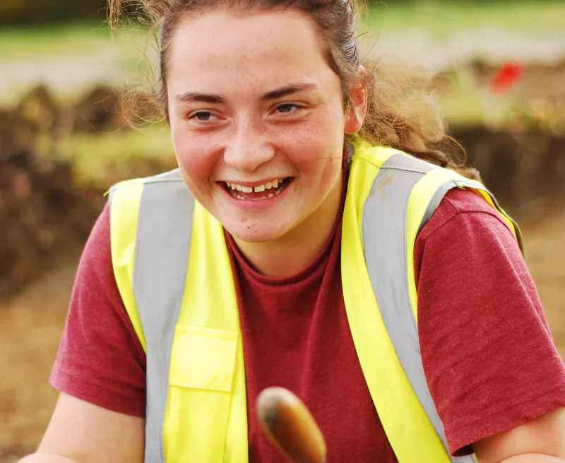 Happy volunteer with their trowel, in a hi-vis vest.