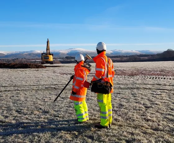 Two archaeologists, one with GPS equipment, staring into the distance in a frozen field