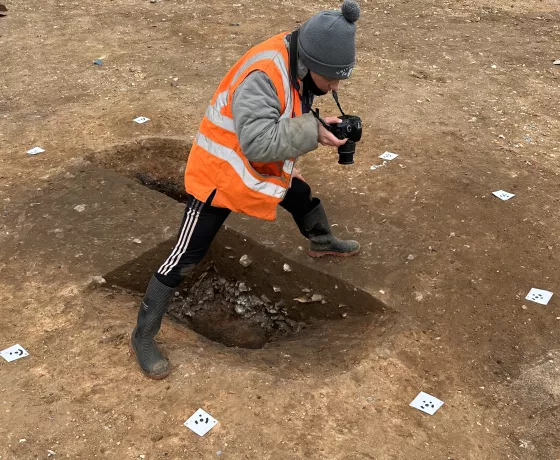 Archaeologist in hi-vis taking photographs of a sunken-feature building